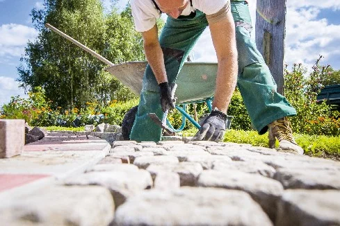 Person verlegt Pflastersteine mit Gummihammer